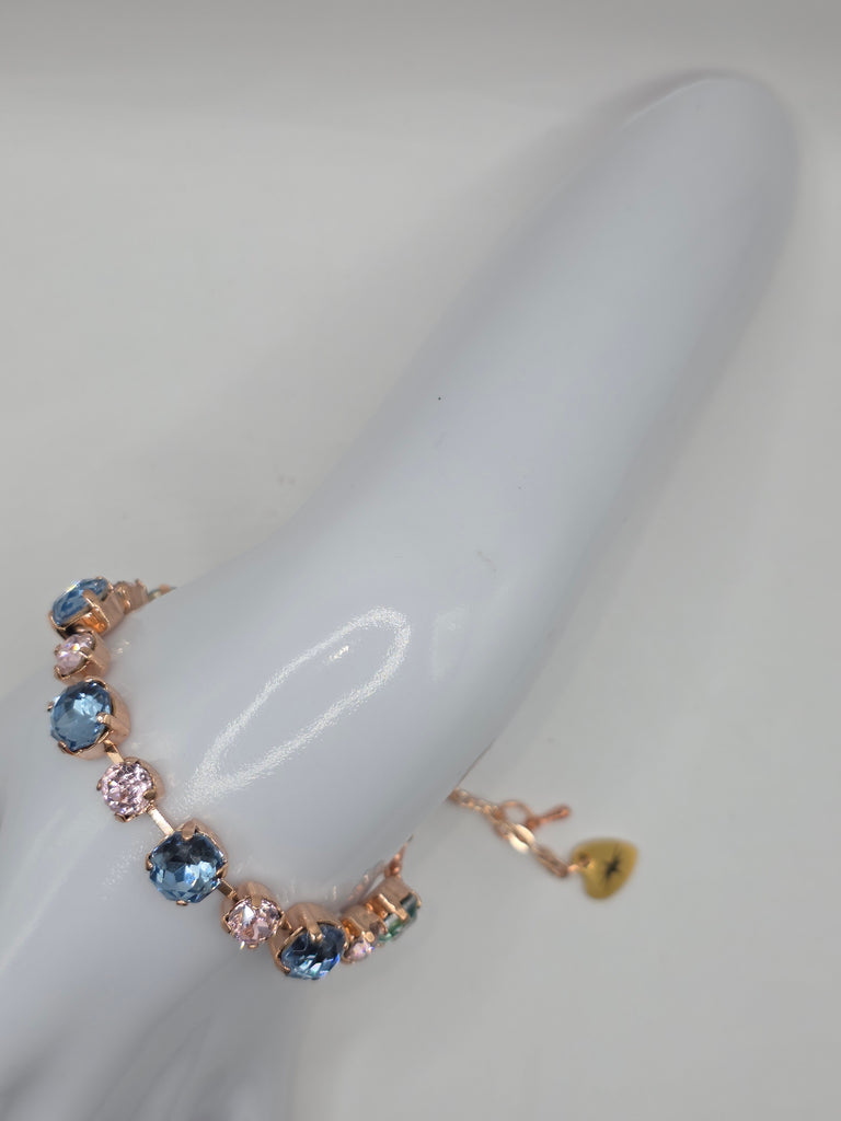 Gold bracelet with blue and pink gemstones on a white stand